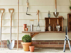 assorted gardening tools leaning against or hanging from a wall
