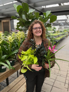 Melissa Woodard in a greenhouse, holding several tropical plants