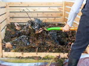 A person using a garden fork to turn compost in a bin.